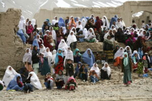 Hazara women and girls in Bamiyan province in the late 2000s, sitting in a large group on and around crumbling walls, with mountains patched with snow in the background. (Photo by Muzafar Ali, courtesy of the authors)